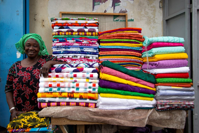Vendor Niouth Fall smiles alongside rows of colourful fabric in Sandaga Market, Avenue Lamine Gueye, Dakar, Senegal, January 25, 2022. Marta Moreiras for StreetNet/ Handout via Thomson Reuters Foundation